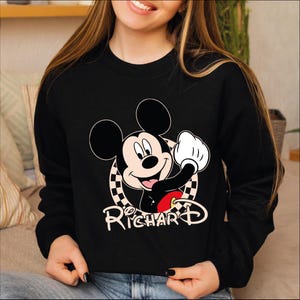 a young girl wearing a mickey mouse sweatshirt