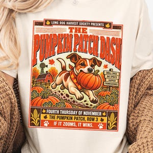 May include: An ivory t-shirt featuring a graphic print of a Jack Russell Terrier carrying a pumpkin in its mouth. The text reads: The Pumpkin Patch Dash, Long Dog Harvest Society Presents, Fourth Thursday of November, The Pumpkin Patch, Row 3, If It Zooms, It Wins.