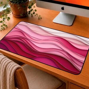 May include: A rectangular desk mat featuring a layered, abstract wave pattern in shades of pink, magenta, and white. The design creates a sense of depth with smooth, flowing curves that transition from deep dark pink to light pastel pink and white.