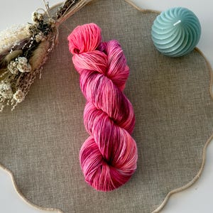 Hilo para calcetines teñido a mano en vibrantes tonos rojos y rosados a partir de una mezcla de lana virgen.