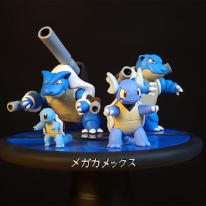 Puede incluir: Un conjunto de figuras Pokémon azules y blancas, incluyendo Blastoise y Squirtle, se exhiben sobre una plataforma azul. Las figuras tienen detalles precisos y se destacan sobre un fondo oscuro. El texto japonés "Mega Mexx" es visible.