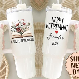 May include: White insulated tumbler with a handle, featuring floral and book graphics, and the text "A New Chapter Begins." The other tumbler says "Happy Retirement" with a heart, name, and year.