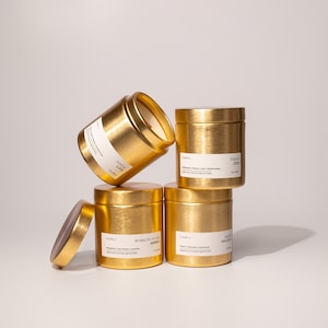 May include: Four gold candle jars with lids. The jars are labeled with the names "Tokyo Zen", "Sparking Winter Bliss", "No. 01 Holiday", and "Save the Date".