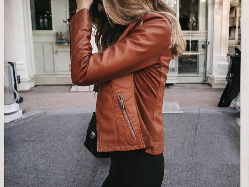 May include: A brown leather jacket with a zip fastening and a zipped pocket on the left side. The jacket is being worn by a person with long blonde hair.