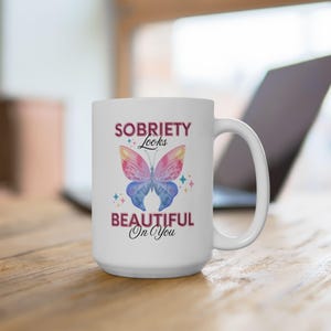 May include: White ceramic coffee mug with a colorful butterfly graphic and the text "Sobriety Looks Beautiful On You".