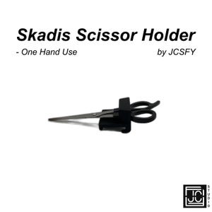 Peut inclure: Support de ciseaux Skadis noir avec une paire de ciseaux. Le texte "Skadis Scissor Holder - One Hand Use by JCSFY" est affiché en haut de l'image. Les ciseaux sont argentés et noirs.