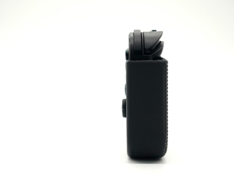 May include: A black rectangular device with a textured surface and a top component. The device has two buttons on the side and a small opening at the top. The background is plain white.