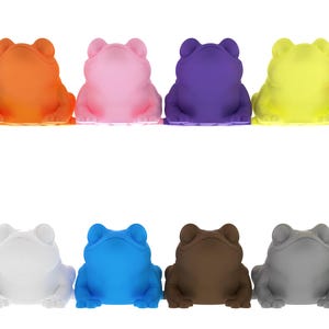 May include: A collection of twelve frog figurines in various colors, including blue, orange, pink, purple, yellow, red, black, white, blue, brown, gray, and green. The frogs are arranged in two rows of six, each with a detailed, textured surface.