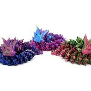 Puede incluir: Tres esculturas con forma de zorros durmiendo, que parecen cristales. Los zorros están hechos de un material iridiscente, uno azul, otro rosa y otro verde.