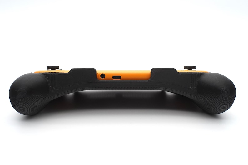 Op de afbeelding: Een zwarte en oranje game controller grip. De grip heeft een gebogen ontwerp met getextureerde handgrepen voor meer comfort. De controller heeft twee zwarte knoppen aan de bovenkant en een oranje middengedeelte. Het ontwerp is strak en modern.