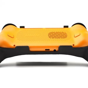 Op de afbeelding: Een oranje en zwarte gaming controller accessoire. De controller heeft een getextureerde oranje achterkant met zwarte handgrepen aan elke kant. Het ontwerp bevat een ventilatieopening en diverse poorten. Het accessoire is ontworpen om de game-ervaring te verbeteren.