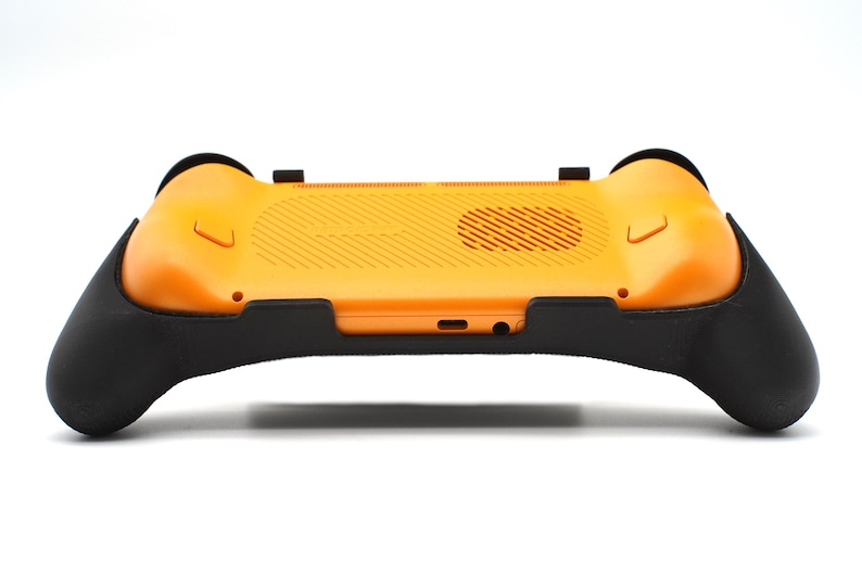 Op de afbeelding: Een oranje en zwarte gaming controller accessoire. De controller heeft een getextureerde oranje achterkant met zwarte handgrepen aan elke kant. Het ontwerp bevat een ventilatieopening en diverse poorten. Het accessoire is ontworpen om de game-ervaring te verbeteren.