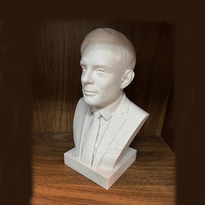May include: A light-colored bust sculpture of a man in a suit and tie. The sculpture is on a rectangular base with text. The bust is a detailed representation of the man's face and upper body.