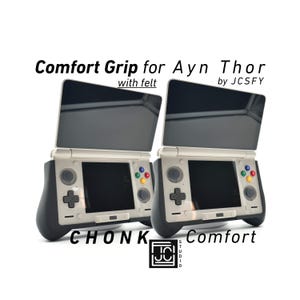 May include: Two Ayn Thor handheld gaming consoles with attached comfort grips. The consoles are white and black with a black screen and colorful buttons. The text "Comfort Grip for Ayn Thor" is visible.
