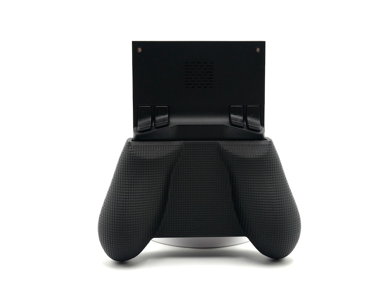 May include: A black handheld gaming device with a textured grip. The device has a screen mount and two ergonomic handles. The design is modern and sleek, suitable for gaming enthusiasts.