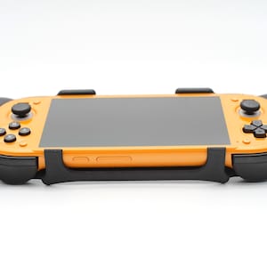 Op de afbeelding: Oranje draagbare gameconsole met een zwart scherm en zwarte accenten. De console heeft knoppen en joysticks. Het apparaat is ontworpen om te gamen.