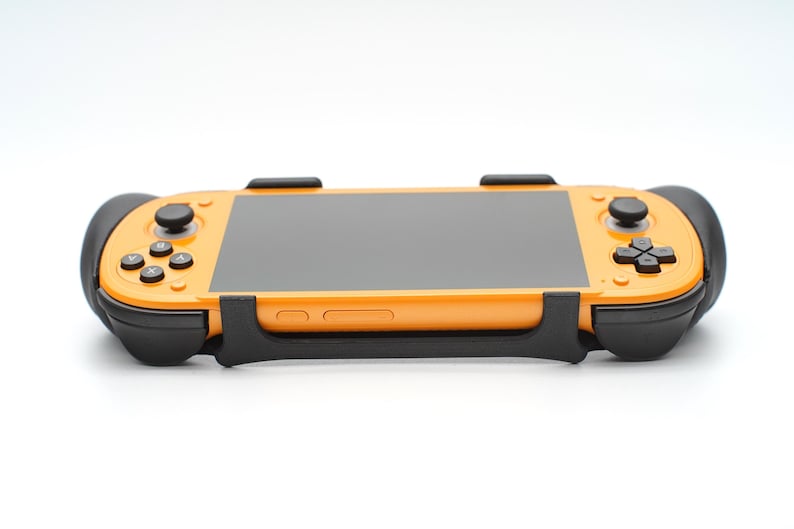Op de afbeelding: Oranje draagbare gameconsole met een zwart scherm en zwarte accenten. De console heeft knoppen en joysticks. Het apparaat is ontworpen om te gamen.