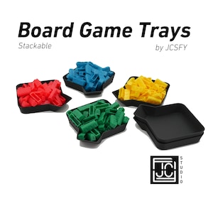 May include: Stackable board game trays in red, blue, green, and yellow. The trays are made of black plastic and have a unique shape. The text "Board Game Trays" and "Stackable" are visible in the image. The text "by JCSFY" is also visible in the image.