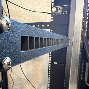 Könnte beinhalten: Ein schwarzes, strukturiertes Rack-Montagepanel mit mehreren rechteckigen Öffnungen. Das Panel ist mit silbernen Schrauben befestigt und Teil eines Server-Rack-Systems. Die Abbildung zeigt eine Nahaufnahme des Panels.