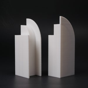 May include: Two white geometric sculptures with rounded edges. The sculptures are made of a smooth, white material and have a modern, minimalist design.