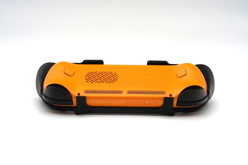 Op de afbeelding: Een oranje en zwarte gameconsole grip, gezien vanaf de achterkant. De grip heeft een getextureerd oranje oppervlak met zwarte handgrepen en een zwarte ondersteuningsstructuur. Het ontwerp bevat ventilatie- en knopdetails.
