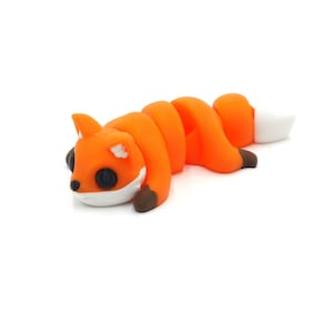 Puede incluir: Figurita de zorro naranja hecha a mano con cola y detalles blancos. El zorro tiene ojos negros y patas marrones. El zorro está tumbado sobre una superficie blanca.