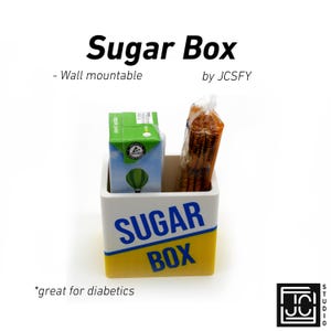 May include: A white and yellow sugar box with the words "SUGAR BOX" in blue. The box contains a small apple juice box and a package of sugar sticks. The text "- Wall mountable" and "by JCSFY" are also visible.