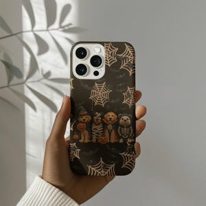 May include: A dark brown phone case featuring a Halloween design. The case has illustrations of dogs dressed in costumes, including a witch, mummy, and skeleton. Spiderwebs and bats are also featured in the design.