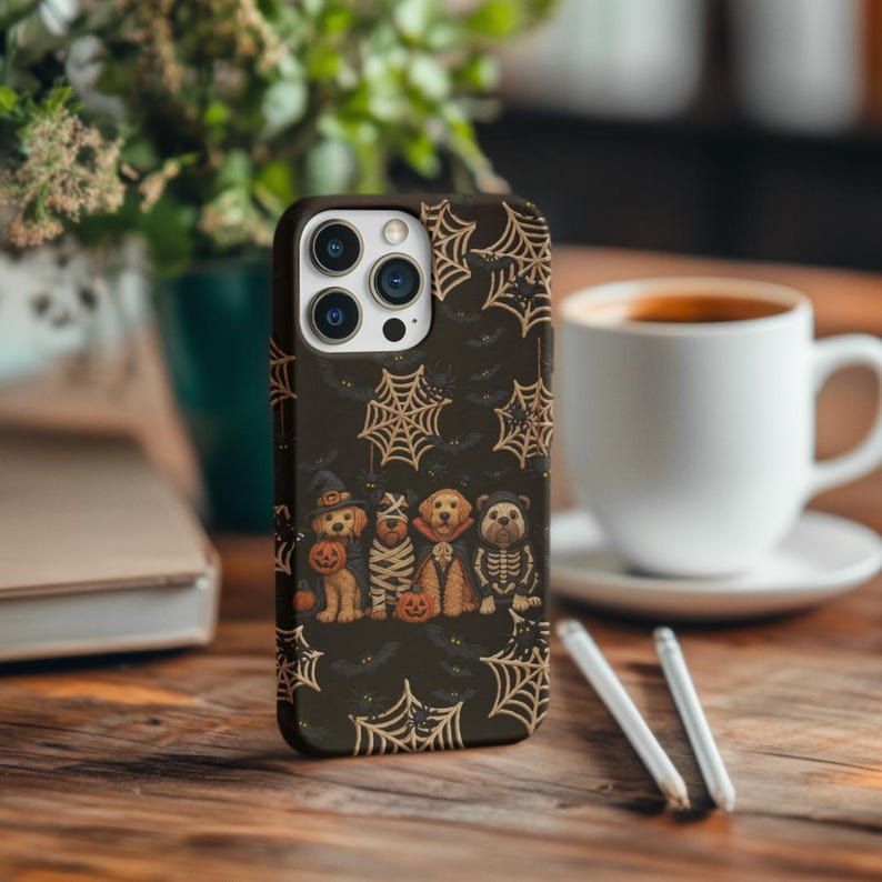 May include: A dark brown phone case featuring a Halloween-themed design. The case has a pattern of spiderwebs and bats. The bottom of the case features a row of dogs dressed in Halloween costumes, including a witch, mummy, and skeleton.