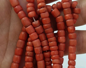 May include: A strand of coral beads, with a natural, reddish-orange color. The beads are cylindrical in shape and have a slightly rough texture. The beads are strung on a white thread.