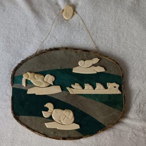 May include: A carved wooden plaque with a green and brown background. The plaque features five ivory carvings of arctic animals, including a walrus, a seal, and three polar bears. The plaque is hanging from a string.