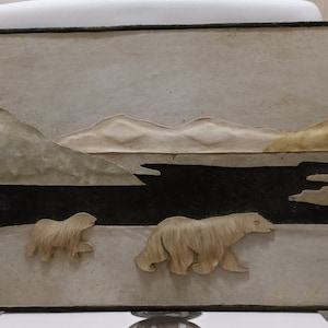 Könnte beinhalten: Ein beige-brauner Wandbehang mit schwarzem Rand. Der Wandbehang zeigt eine Landschaft mit Bergen, einem Fluss und zwei Eisbären. Die Eisbären sind aus einem strukturierten Material gefertigt, das an Fell erinnert.
