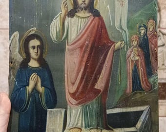 May include: Antique religious icon depicting a central figure with a halo, wearing a red and white robe, and holding a banner. An angel in blue kneels on the left. The icon is painted on a weathered wooden panel.
