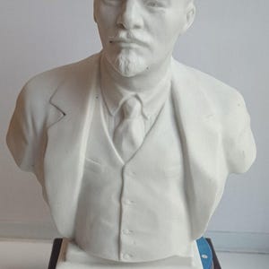 Peut inclure: Un buste en porcelaine blanche d'un homme portant un costume et une cravate. Le buste est posé sur une boîte bleu et blanche avec le mot "NIVEA" imprimé dessus.