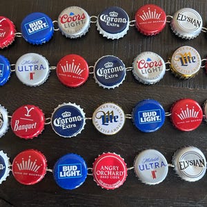 May include: A bracelet made from various beer bottle caps. The caps feature logos for brands such as Bud Light, Coors Light, Corona Extra, and Michelob Ultra. The bracelet is silver and has a clasp.