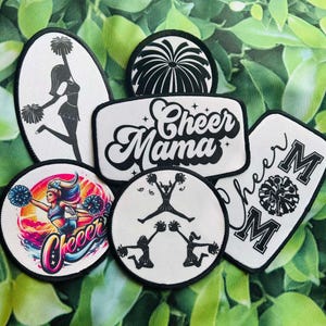 May include: A set of six black and white iron-on patches with cheerleading themes. The patches feature cheerleaders, pom-poms, and the text "Cheer Mama" and "Cheer Mom".