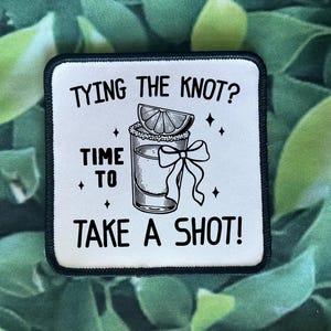 May include: White square patch with black text and a black and white illustration of a shot glass with a lime wedge and a bow. The text reads "TYING THE KNOT? TIME TO TAKE A SHOT!"