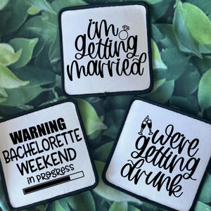 Könnte beinhalten: Drei weiße quadratische Patches mit schwarzem Text und Grafiken. Der erste Patch sagt "i'm getting married" mit einer Diamant-Ring-Grafik. Der zweite Patch sagt "WARNING BACHELORETTE WEEKEND in progress" mit einer Fortschrittsbalken-Grafik. Der dritte Patch sagt "we're getting drunk" mit einer Grafik von zwei Champagnergläsern.