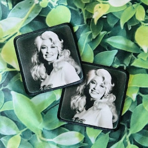 Peut inclure: Deux écussons carrés avec une image en noir et blanc d'une femme souriante aux cheveux blonds. Les écussons ont une bordure noire et sont posés sur un fond de feuilles vertes.