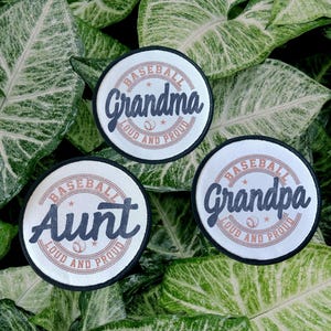 May include: Three round baseball patches with black borders and white backgrounds. The patches read "Grandma", "Aunt", and "Grandpa" in navy blue script, surrounded by "Baseball Loud and Proud" in a circular design.