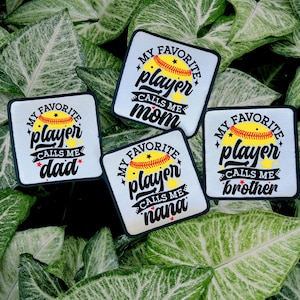 Könnte beinhalten: Vier weiße quadratische Patches mit schwarzen Rändern. Jeder Patch zeigt einen gelben Softball mit roten Nähten und den Text "Mein Lieblingsspieler nennt mich" gefolgt von einem anderen Wort auf jedem Patch: "Mama", "Papa", "Oma" und "Bruder".