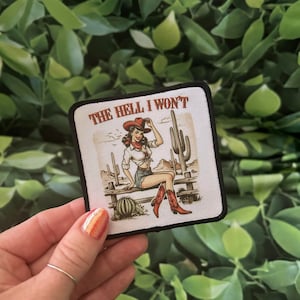 May include: A white patch with black trim features a cartoon illustration of a woman in a red cowboy hat and denim shorts sitting on a fence. The text "THE HELL I WON'T" is printed in black at the top of the patch.