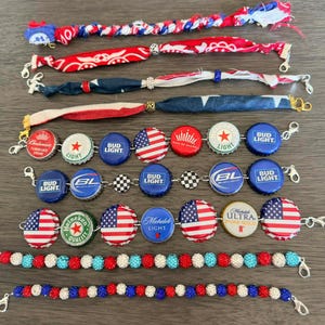 Könnte beinhalten: Eine Sammlung von Armbändern mit patriotischen und Biermotiven. Einige Armbänder zeigen rot-, weiß- und blaue Stoffe, während andere Kronkorken mit amerikanischen Flaggen und Bierlogos verwenden. Zusätzliche Armbänder haben Perlendesigns.