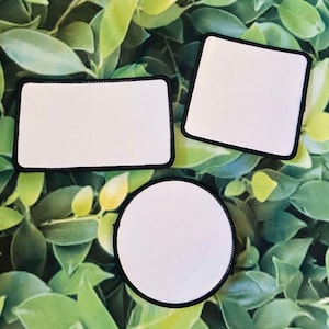 May include: Three white blank patches with black borders, two rectangular and one round, on a green leafy background.