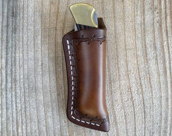 May include: A brown leather knife sheath featuring a stamped barbed wire pattern along the edges and white contrast stitching. The sheath contains a folding pocket knife with a brass bolster and a dark wood handle.