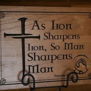 May include: Wooden sign with a black cross and the quote "As Iron Sharpens Iron, So Man Sharpens Man" with the scripture reference "Proverbs 27:17".