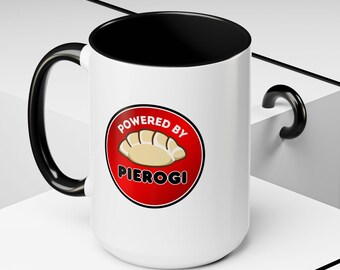 May include: White ceramic mug with a black handle and interior. The mug features a red circle with the words "Powered by Pierogi" and an illustration of pierogi.