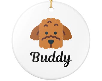 May include: White ceramic ornament with a cartoon dog design. The dog is brown with a mustache and the name "Buddy" in black script. A gold string is attached for hanging.