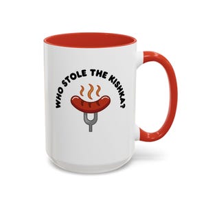 May include: White ceramic mug with a red interior and handle. The mug features the text "WHO STOLE THE KISHKA?" in black, surrounding an illustration of a sausage on a fork. The sausage is brown with steam rising from it.