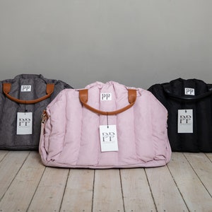 May include: Three quilted nappy bags in grey, pink, and black with brown leather handles and a white tag with the text "PP" on each bag.